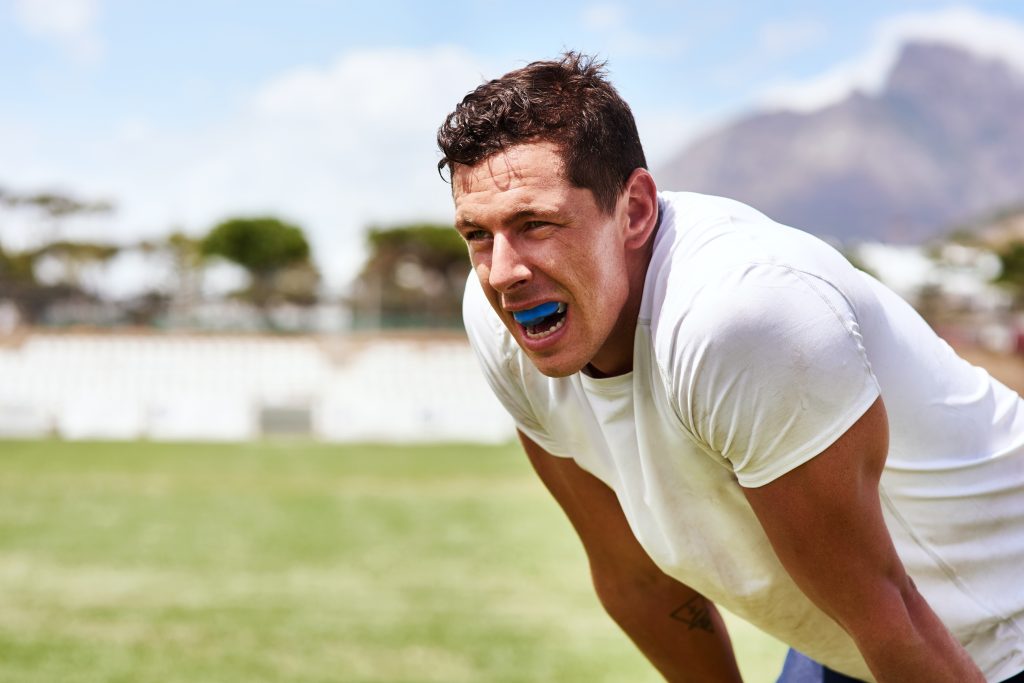 Male athlete wearing a protective mouthguard while playing contact sport with adult braces, metal braces or ceramic braces.