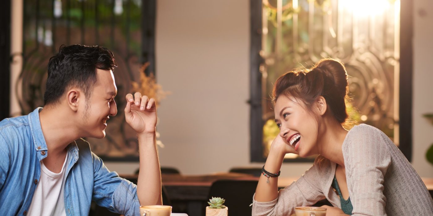Side view portrait of laughing Asian couple enjoying date in cafe