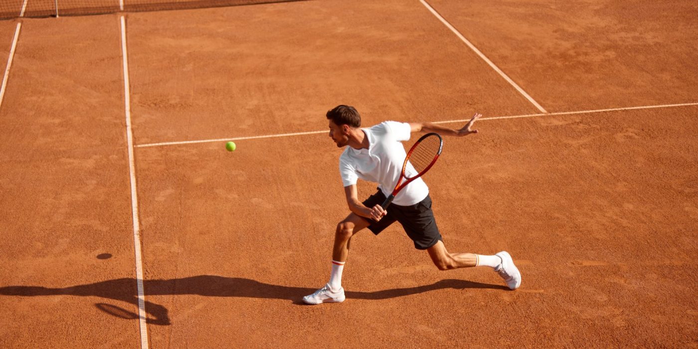 Young man, tennis player showing endurance and strength during intensive training on clay court. Man practicing for upcoming game. Concept of sport, competition, active and healthy lifestyle