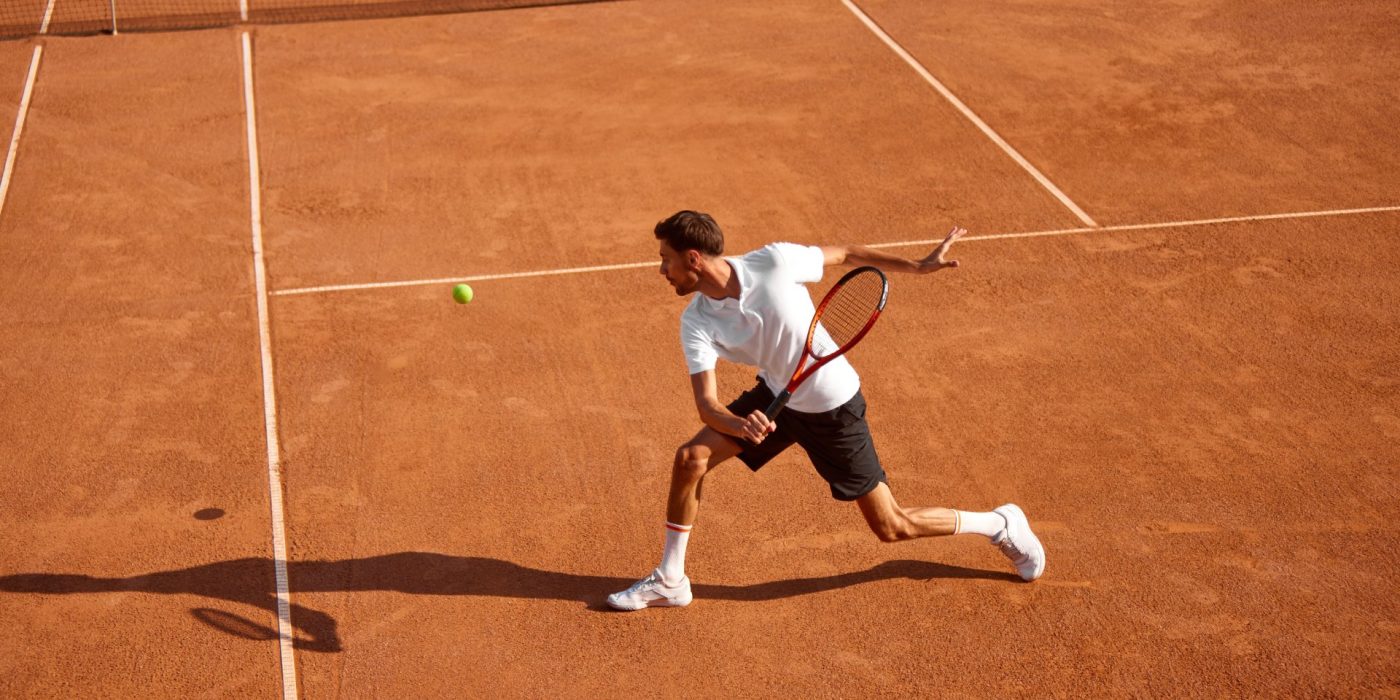 Young man, tennis player showing endurance and strength during intensive training on clay court. Man practicing for upcoming game. Concept of sport, competition, active and healthy lifestyle