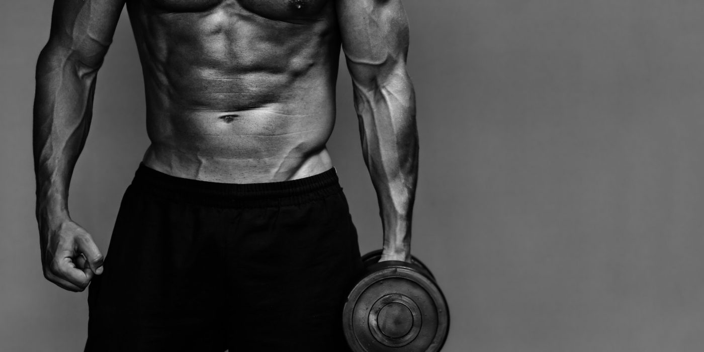 Close up of muscular bodybuilder guy doing exercises with weights over grey background. Black and white