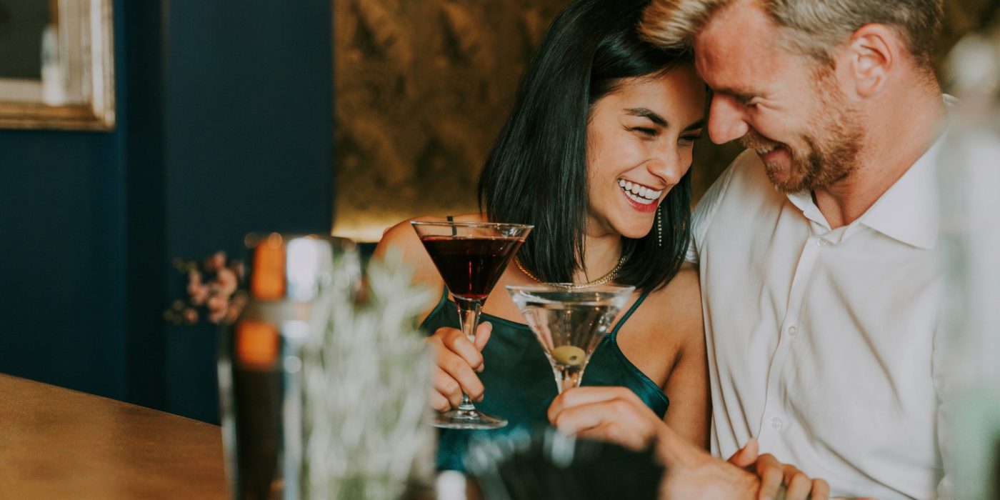 Happy couple in love drinking cocktail glasses sitting at bar counter - Boyfriend and girlfriend having romantic date outdoors - Beverage and lovers concept